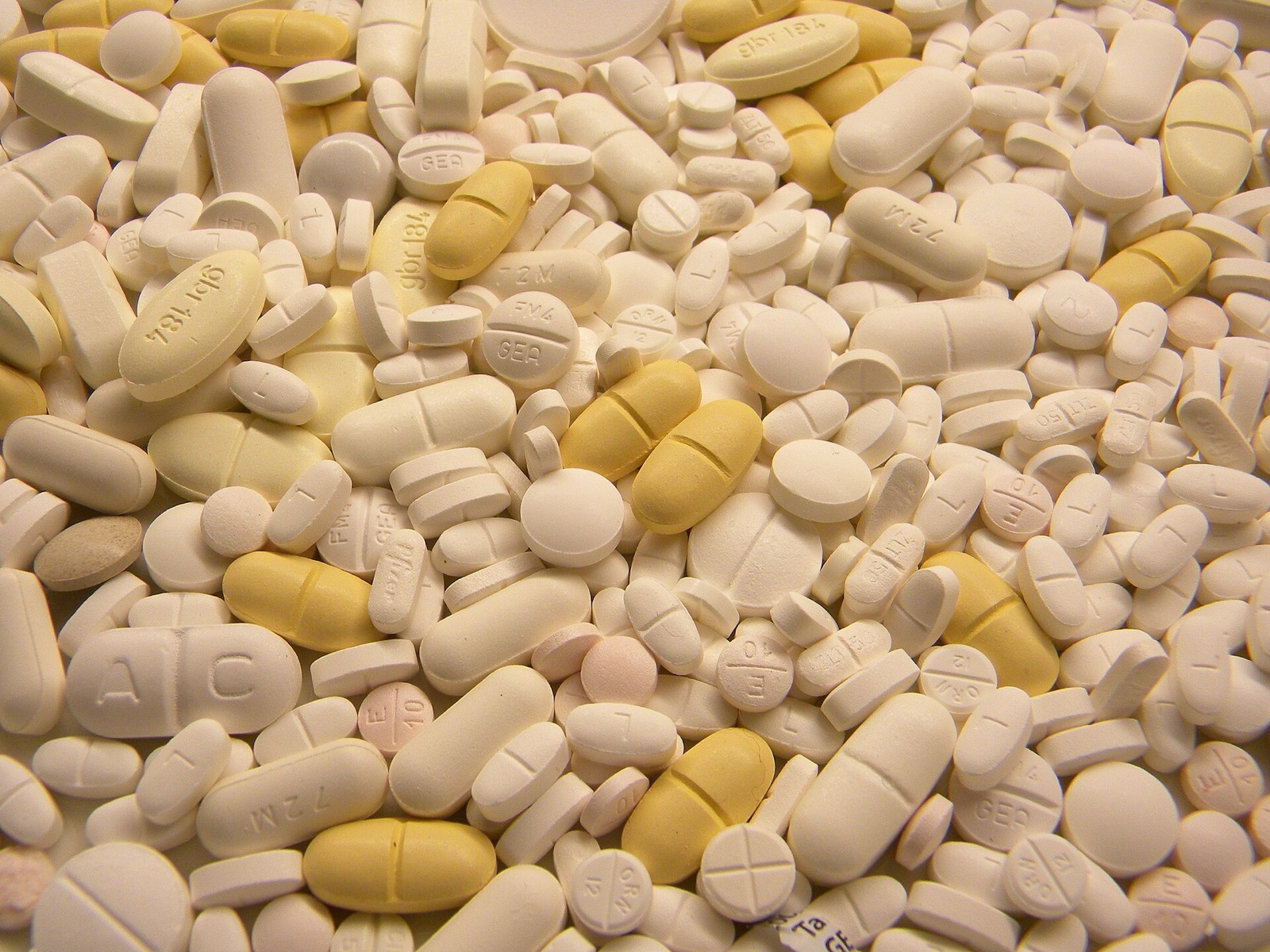 A dense field of white and yellow pharmaceutical tablets filling the frame