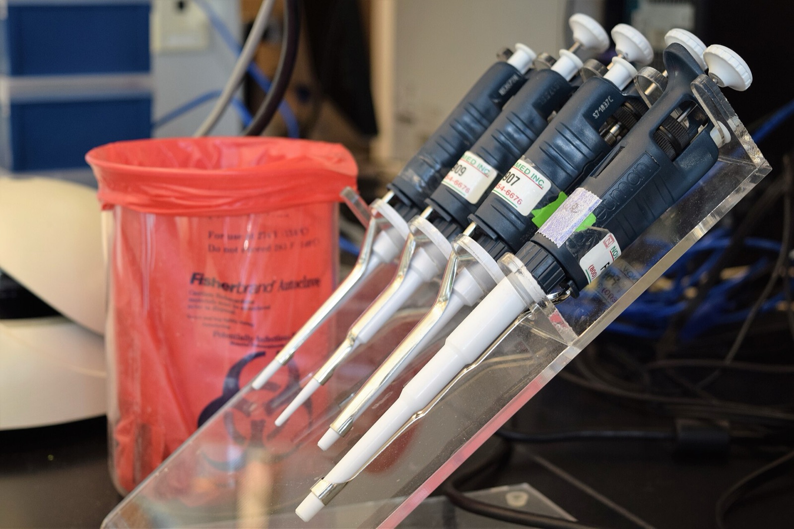 A rack of laboratory micropipettes beside a red biohazard waste bin