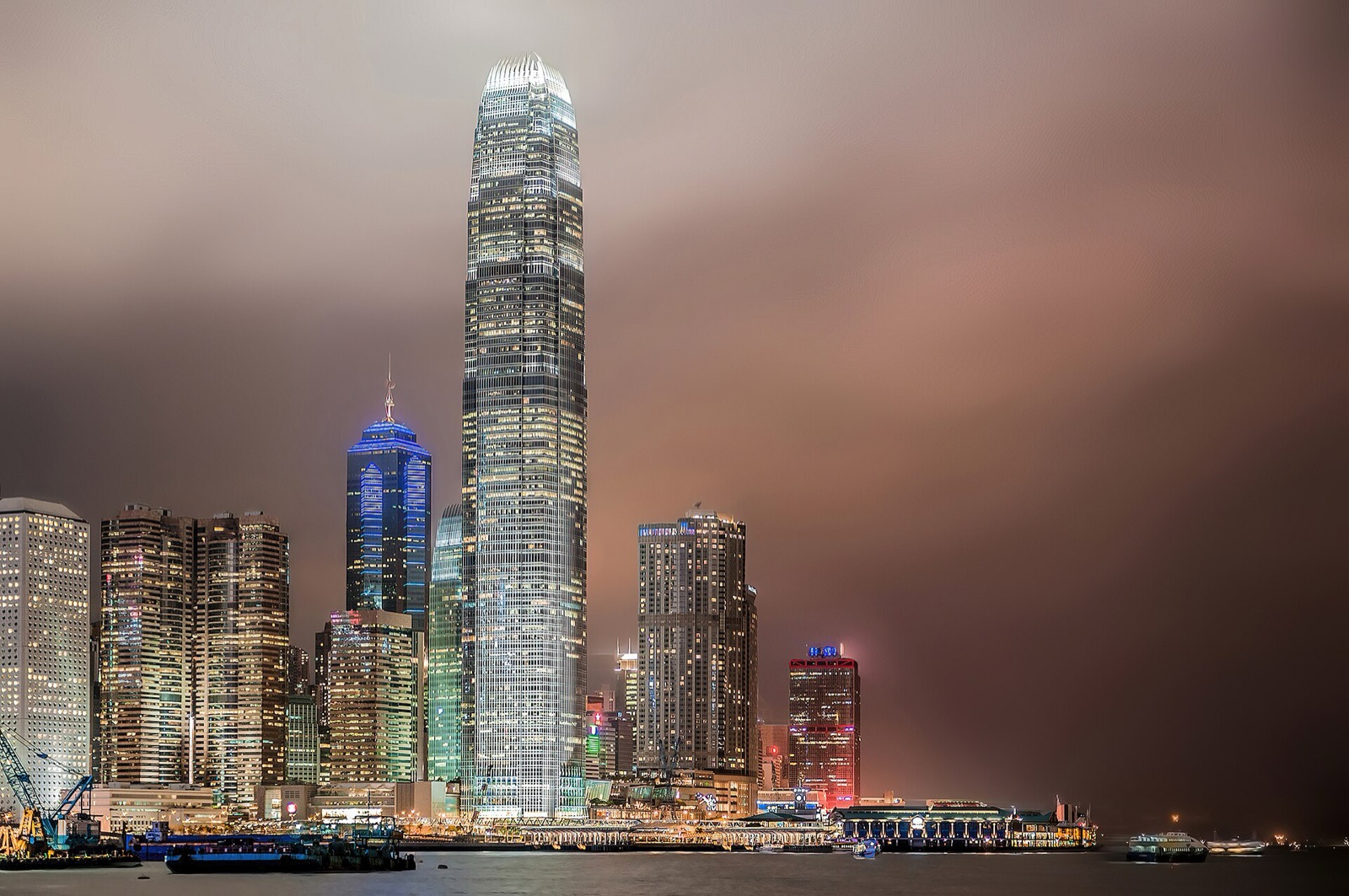 Hong Kong's financial district at night, a single tower rising above the harbour into low cloud