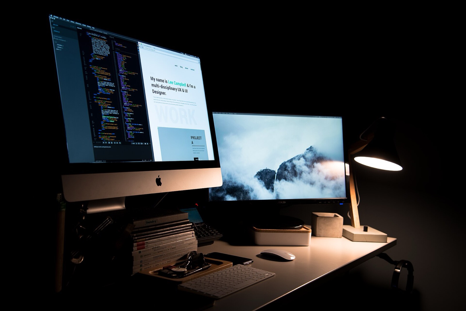 A desk lit only by two monitors and a small lamp, code open on the left screen