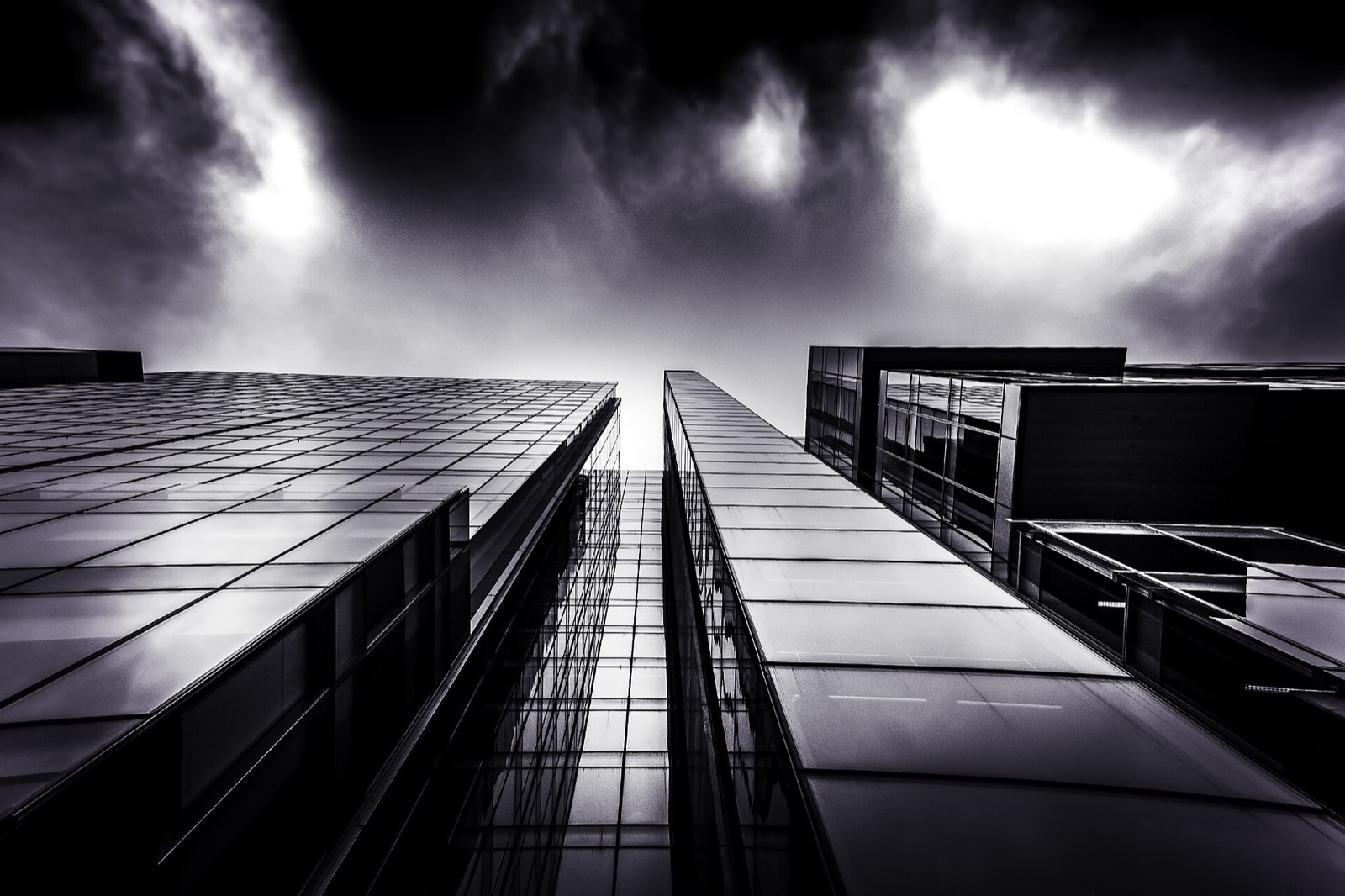 Looking straight up between two black glass towers into a storm sky