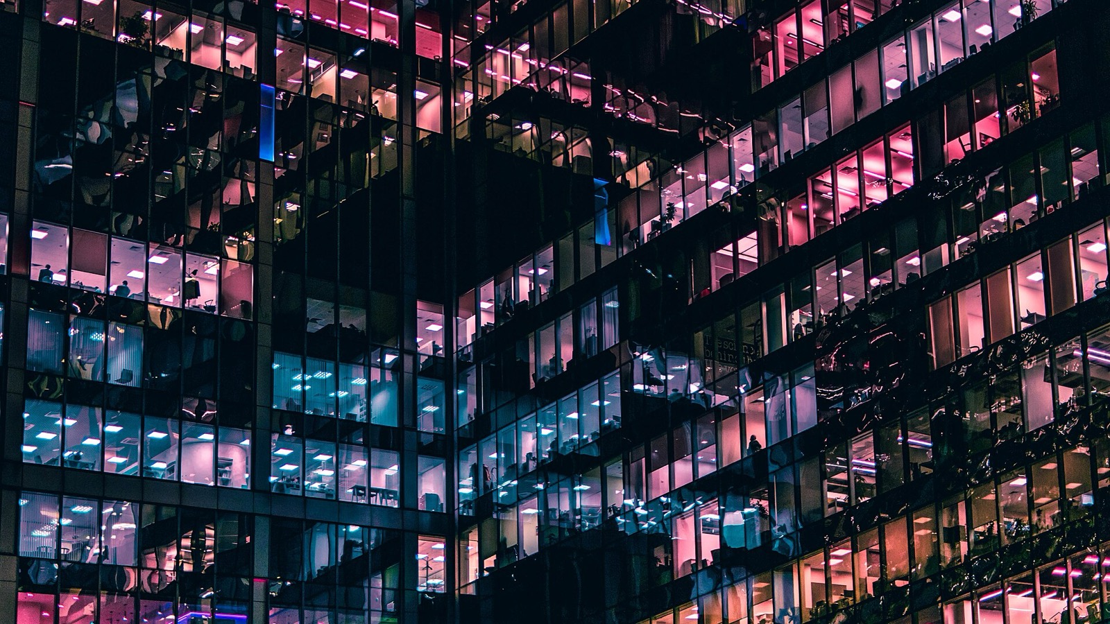 A tower of office windows at night, each lit a different colour, most of them empty