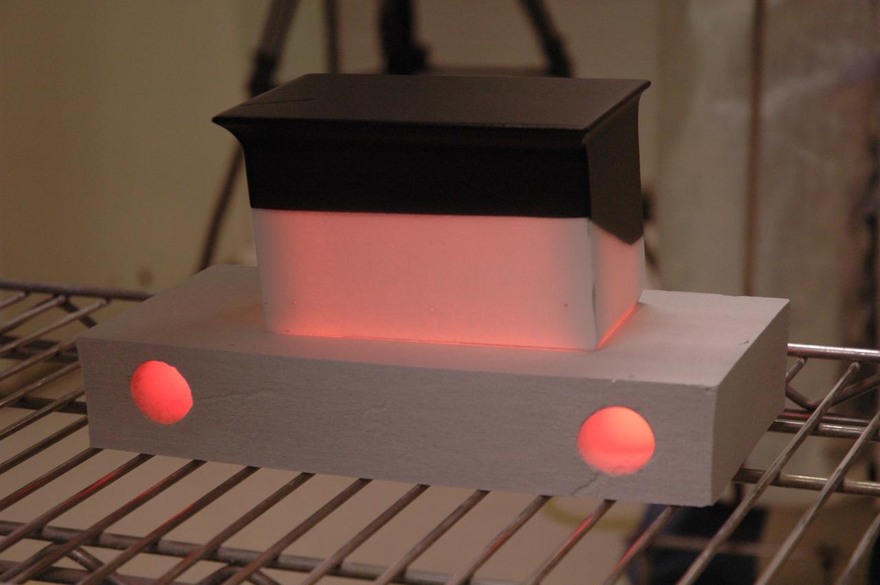 A Shuttle tile still glowing red on a rack after coming out of a 2,200°F oven