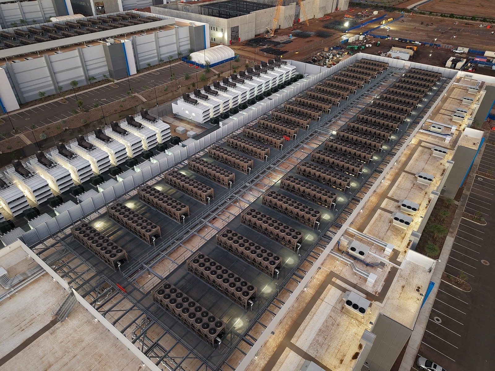 Aerial view at dusk of a hyperscale data center under construction in the desert, its cooling plant and backup generators laid out in long rows