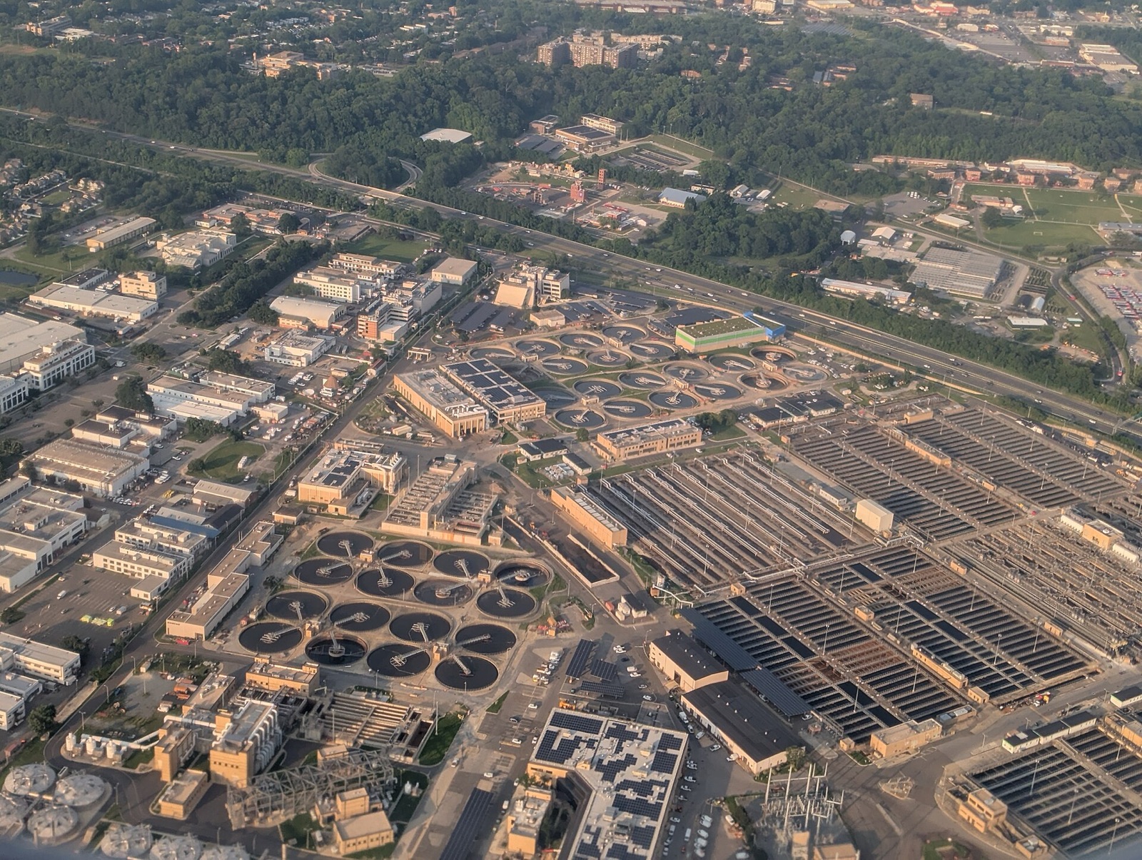 Aerial view of a vast wastewater treatment plant, dozens of circular clarifiers and long rectangular basins covering an entire urban district