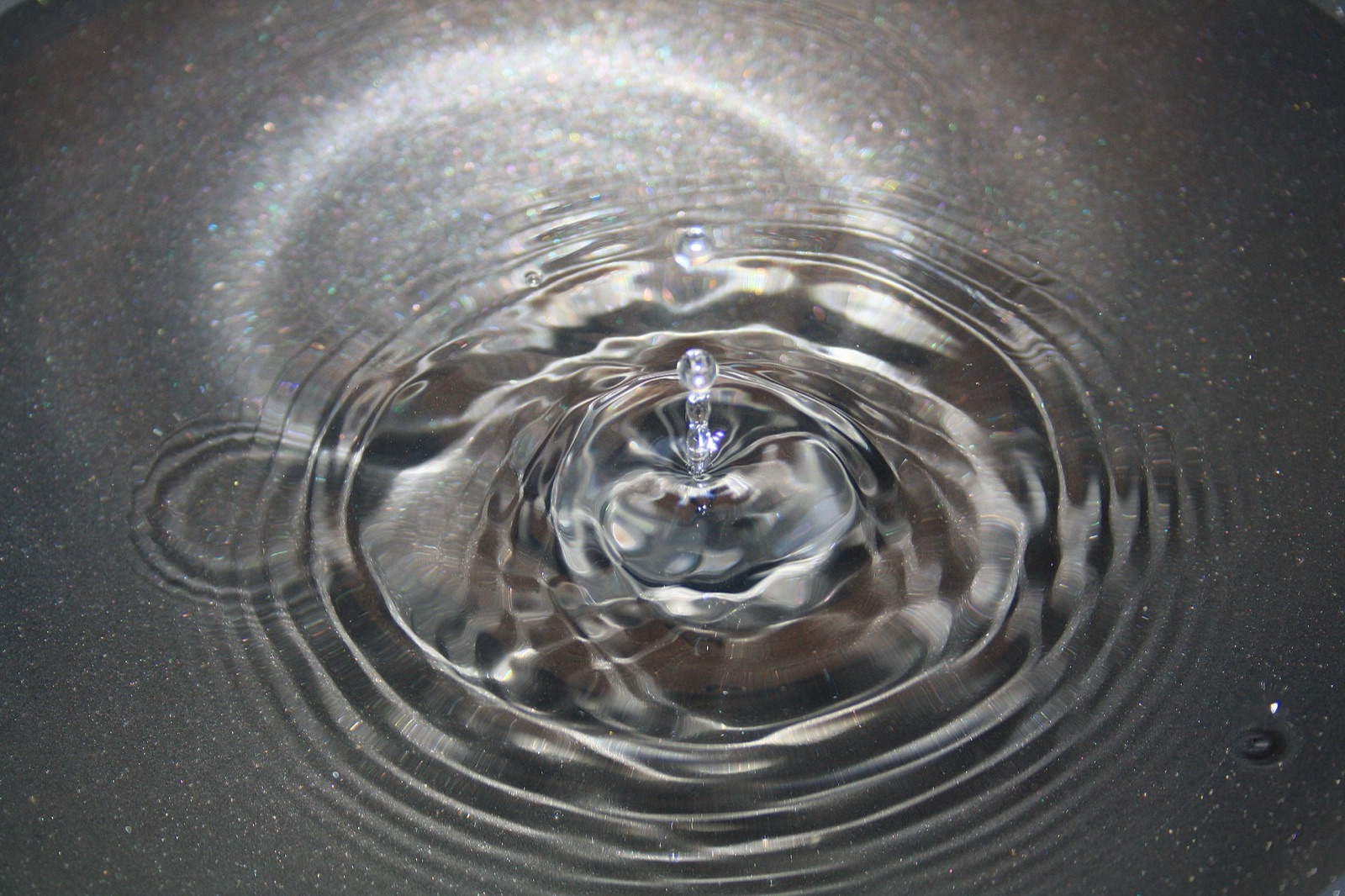 Macro photograph of a single water droplet rebounding from a still surface, concentric ripples spreading outward