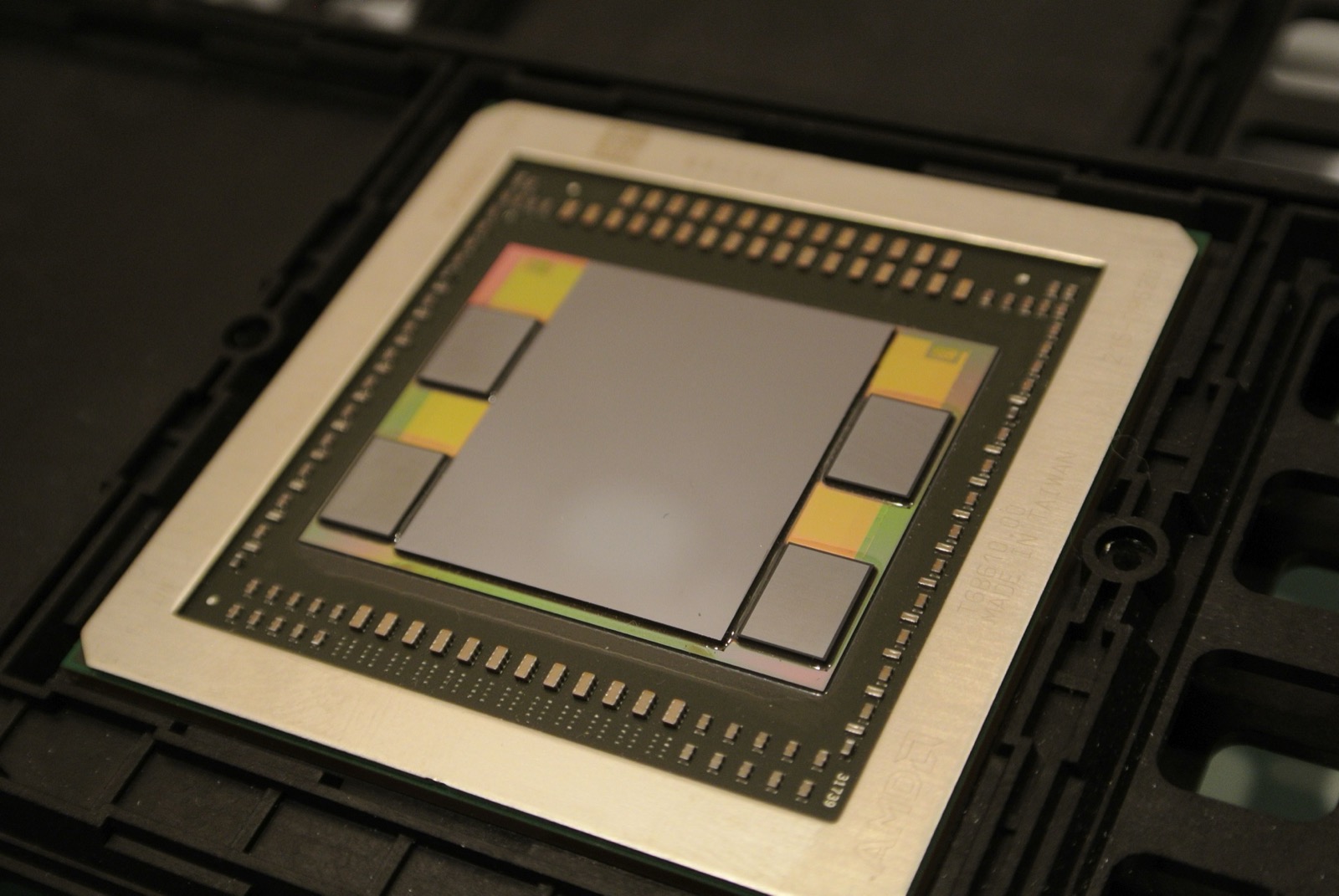 An AMD Fiji GPU package. The large square die in the center is the processor; the four rectangular slabs hugging it are stacks of High Bandwidth Memory, all mounted on a shared slice of silicon called an interposer.