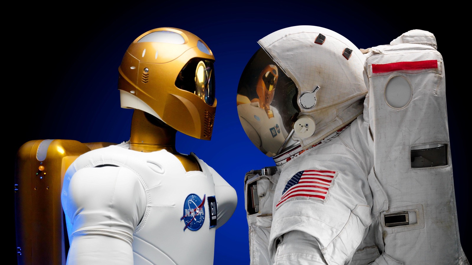 NASA's Robonaut 2 humanoid stands face-to-face with an empty astronaut spacesuit, the robot's golden helmet reflected in the human visor.